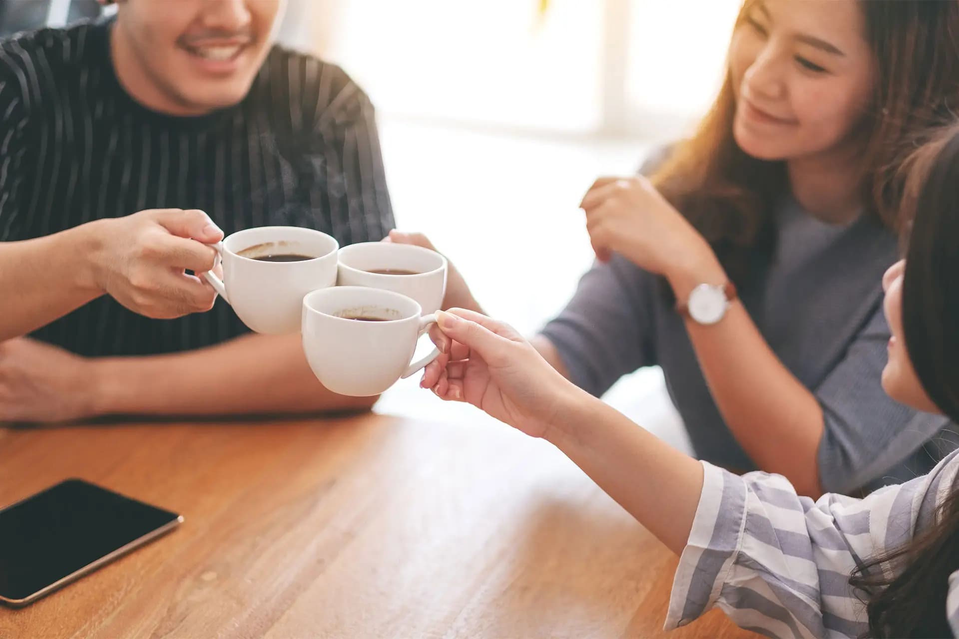 Tres personas brindando con tazas de café alrededor de una mesa